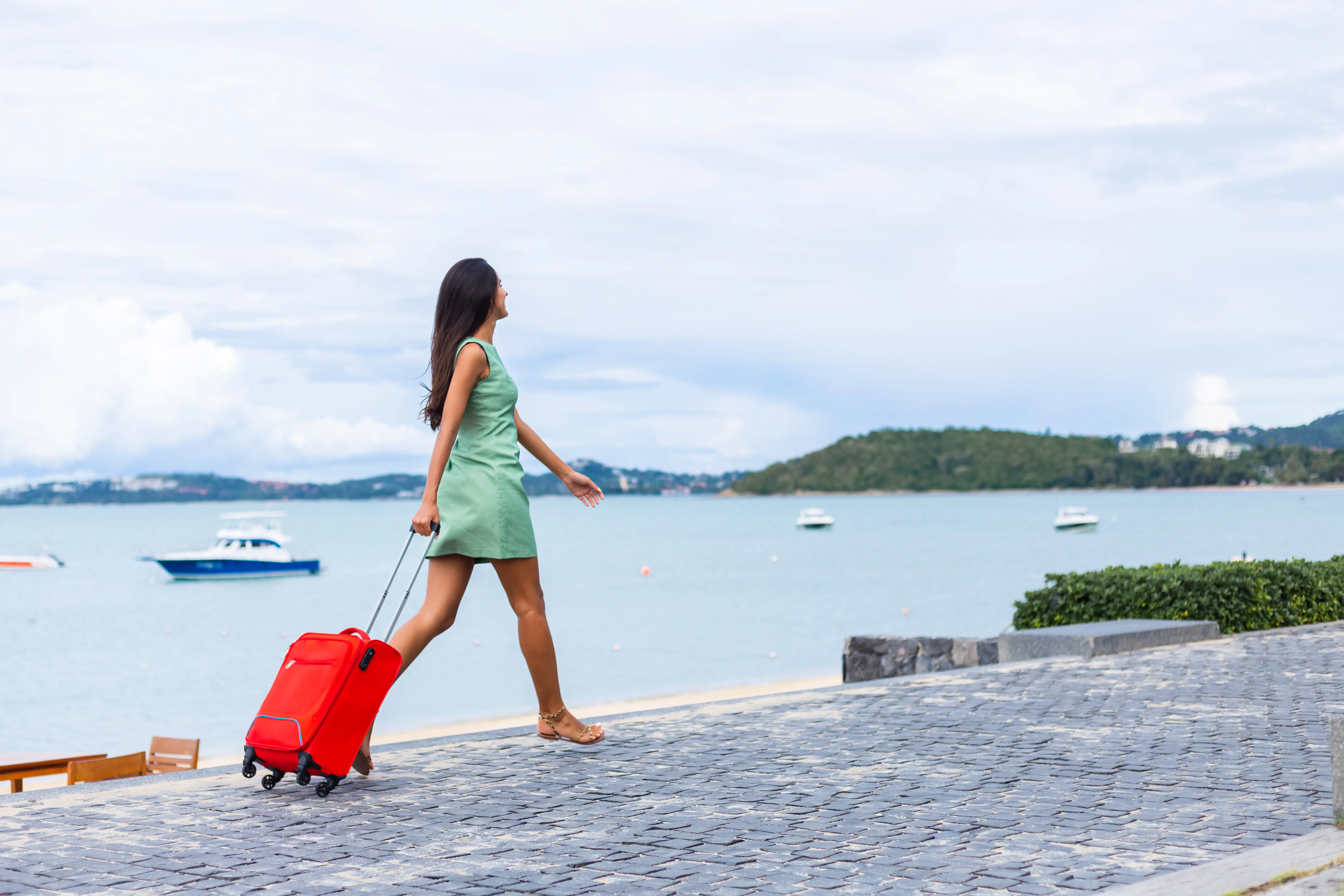 a woman walking on the beach with a red suitcase